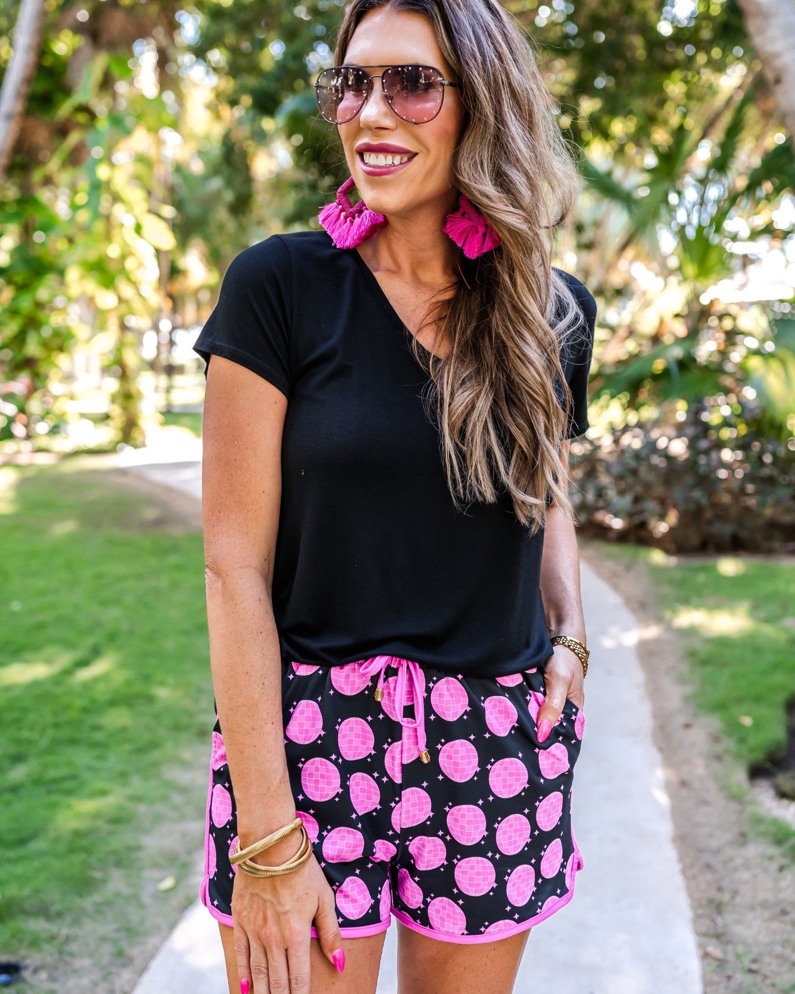mid-rise relaxed fit activewear shorts with side pockets and a tie waist drawstring with gold bead accents, designed on a pink disco and stars pattern print fabric, black base, and pink trim