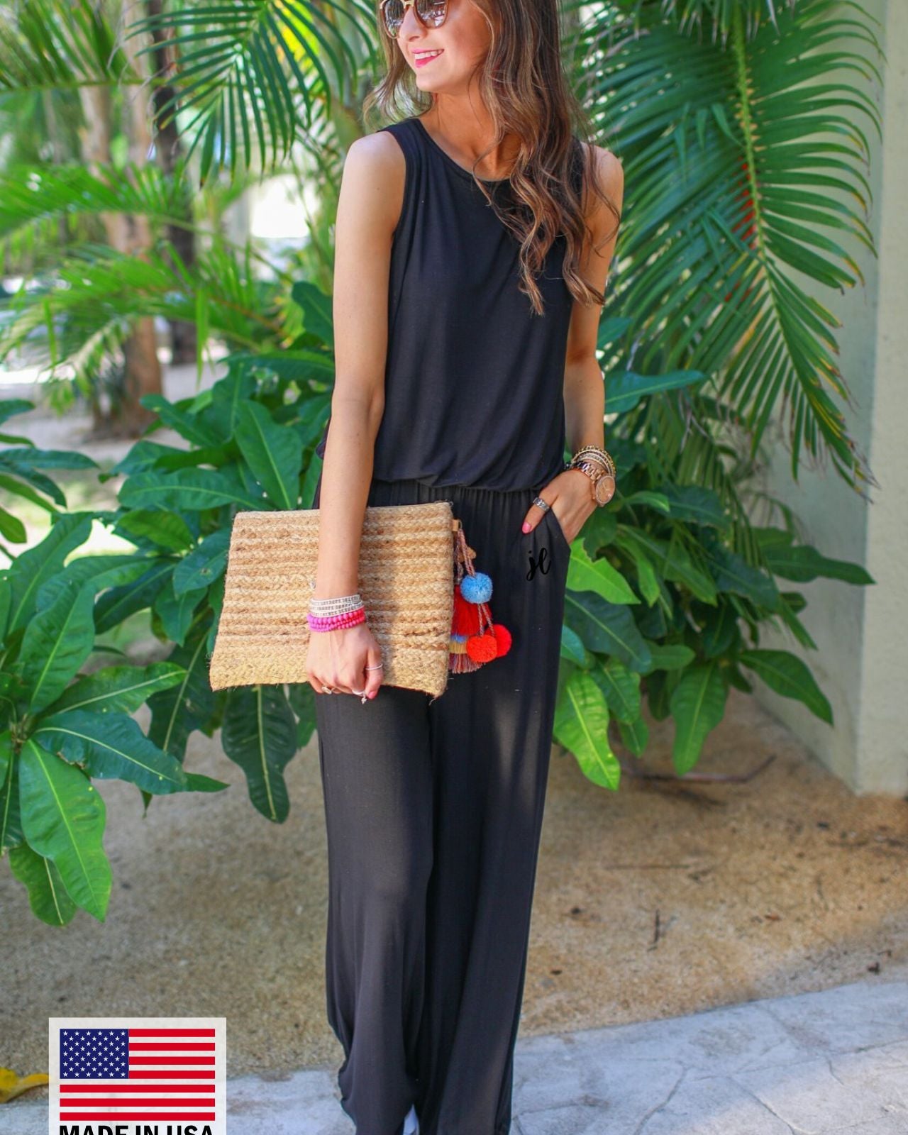 a black sleeveless one-piece jumpsuit with wide 2.5" shoulder straps, a rounded neckline, elastic waist, side pockets, keyhole button back, and a relaxed flare leg silhouette, accented with a MADE IN USA watermark in bottom left-hand corner