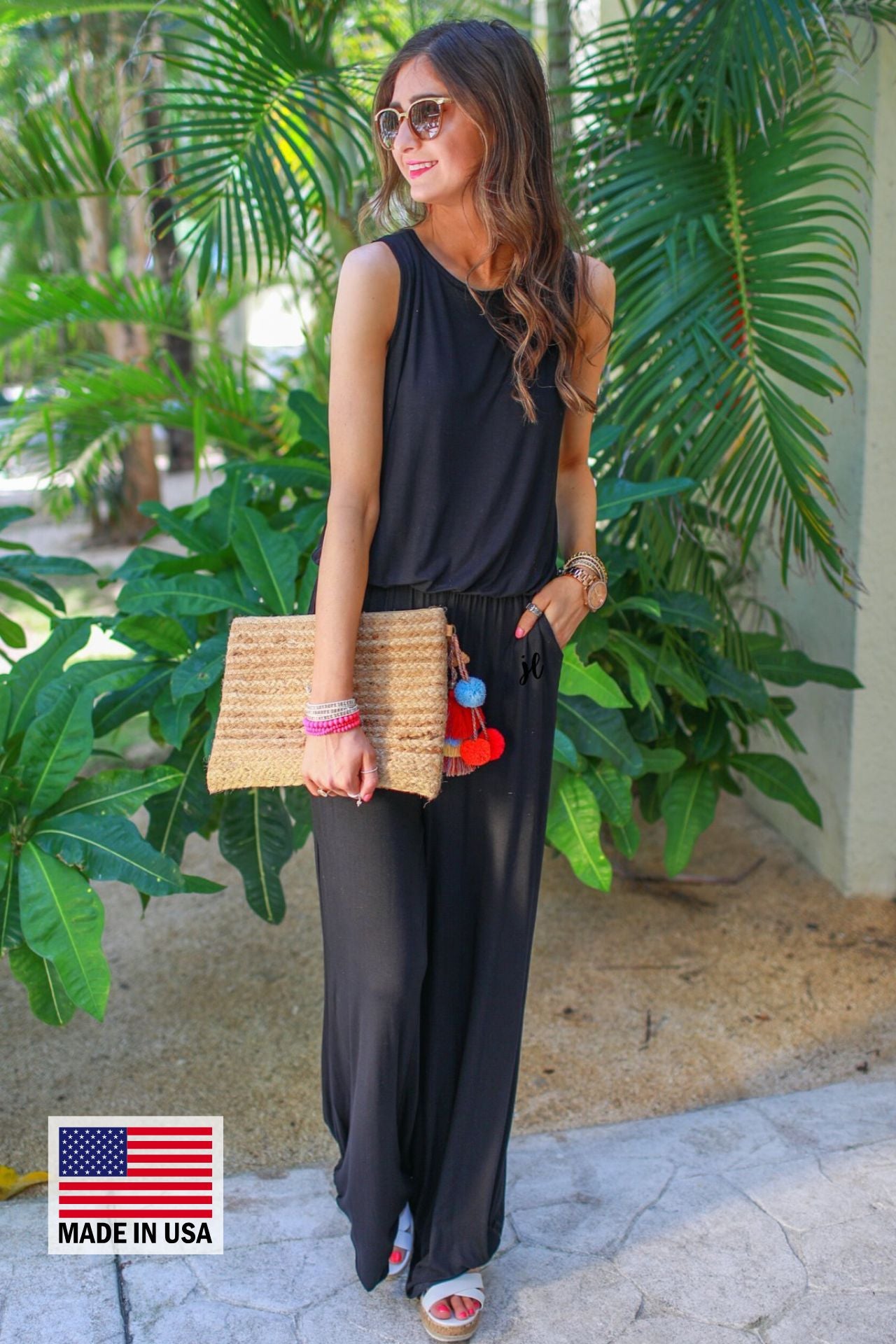 a black sleeveless one-piece jumpsuit with wide 2.5" shoulder straps, a rounded neckline, elastic waist, side pockets, keyhole button back, and a relaxed flare leg silhouette, accented with a MADE IN USA watermark in bottom left-hand corner