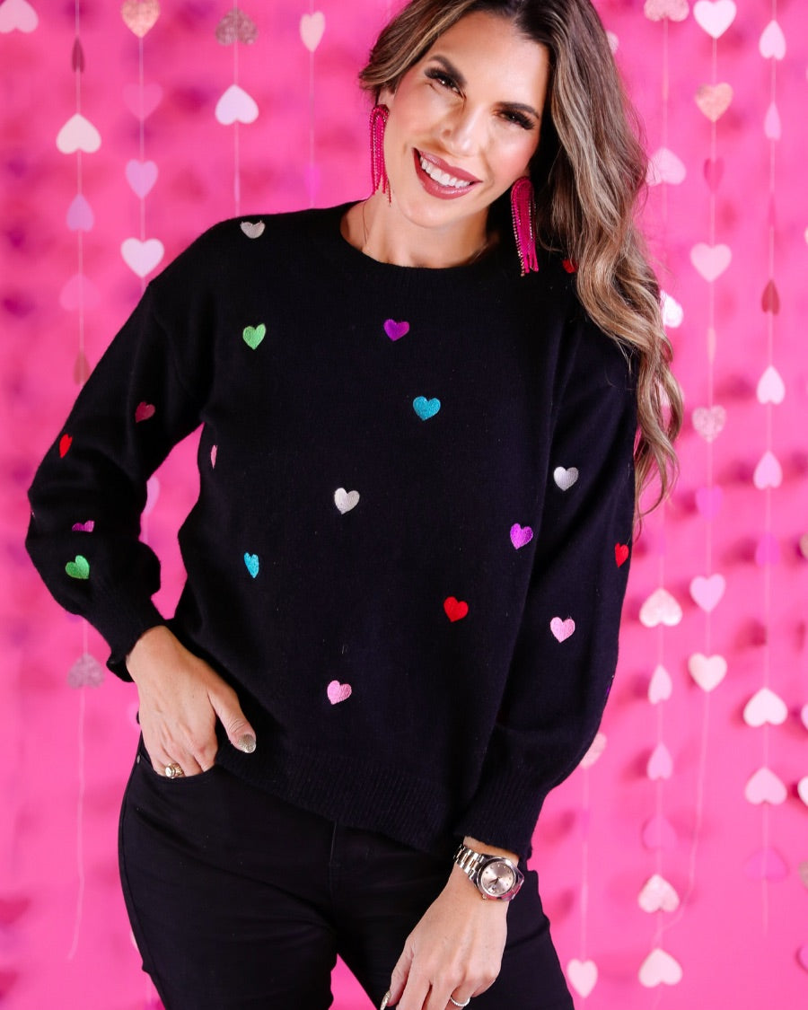 a black long-sleeve sweater crafted from snug, plush material adorned with colorful embroidered hearts, finished with ribbed trim on the neckline, cuffs, and hem