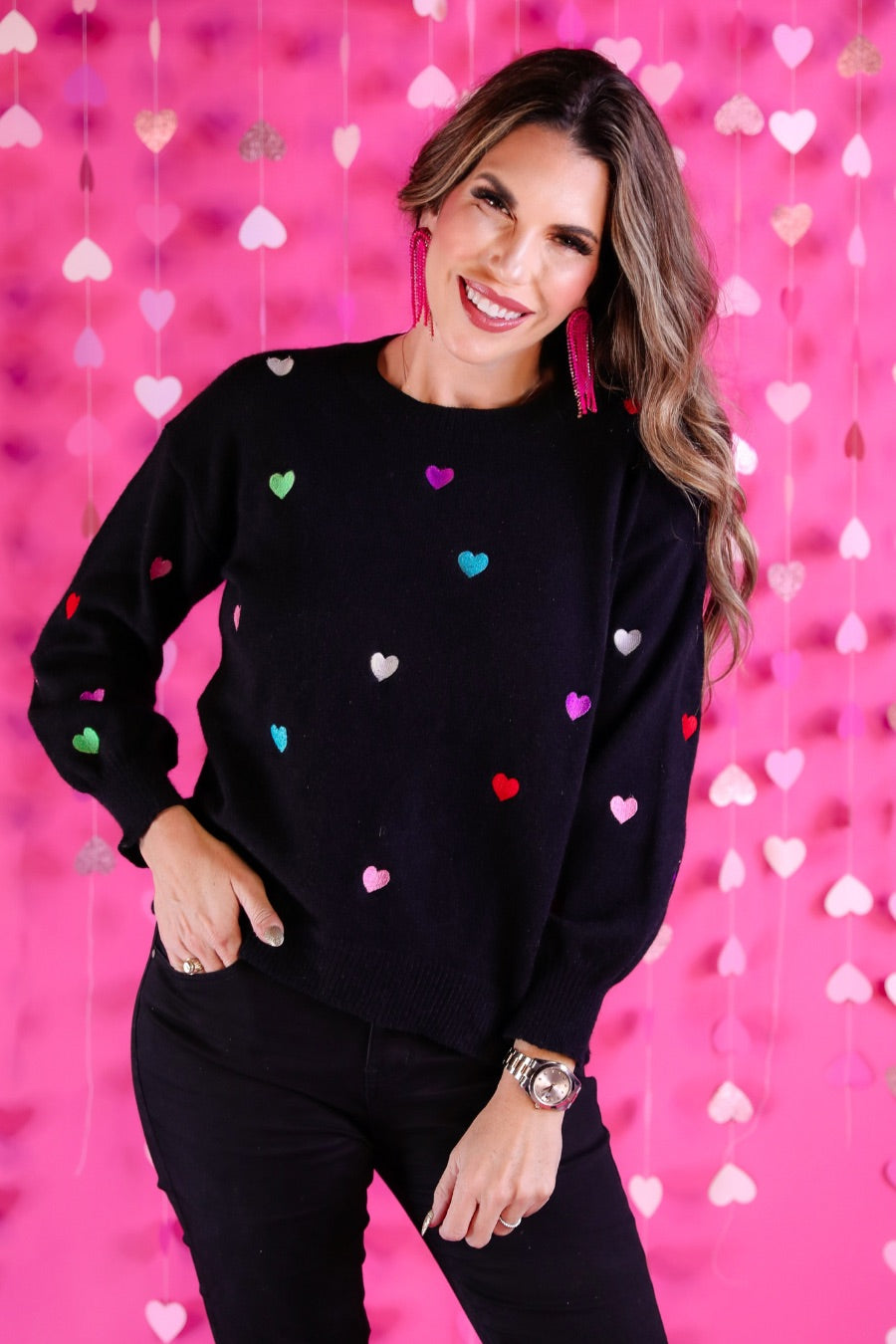 a black long-sleeve sweater crafted from snug, plush material adorned with colorful embroidered hearts, finished with ribbed trim on the neckline, cuffs, and hem
