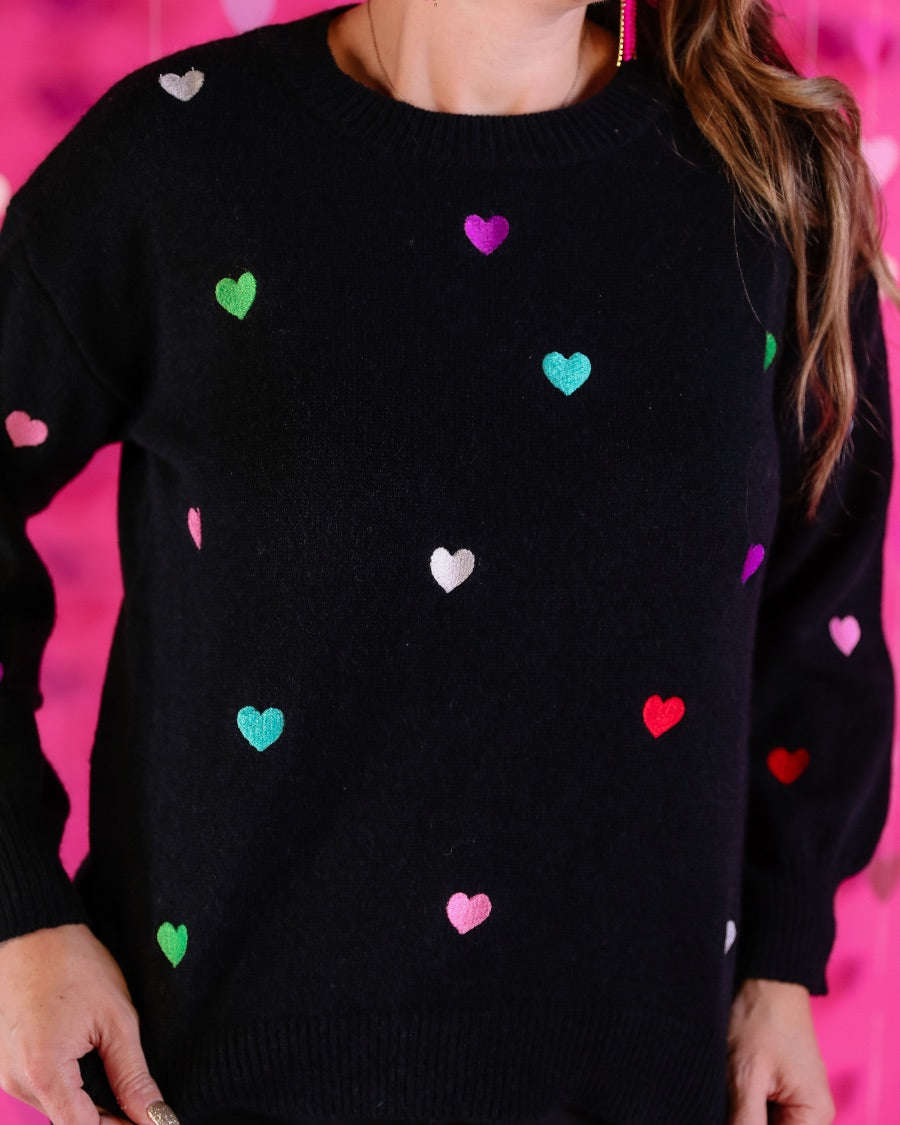 a black long-sleeve sweater crafted from snug, plush material adorned with colorful embroidered hearts, finished with ribbed trim on the neckline, cuffs, and hem