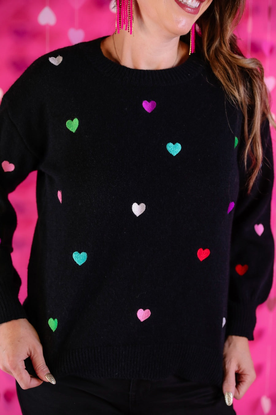 a black long-sleeve sweater crafted from snug, plush material adorned with colorful embroidered hearts, finished with ribbed trim on the neckline, cuffs, and hem