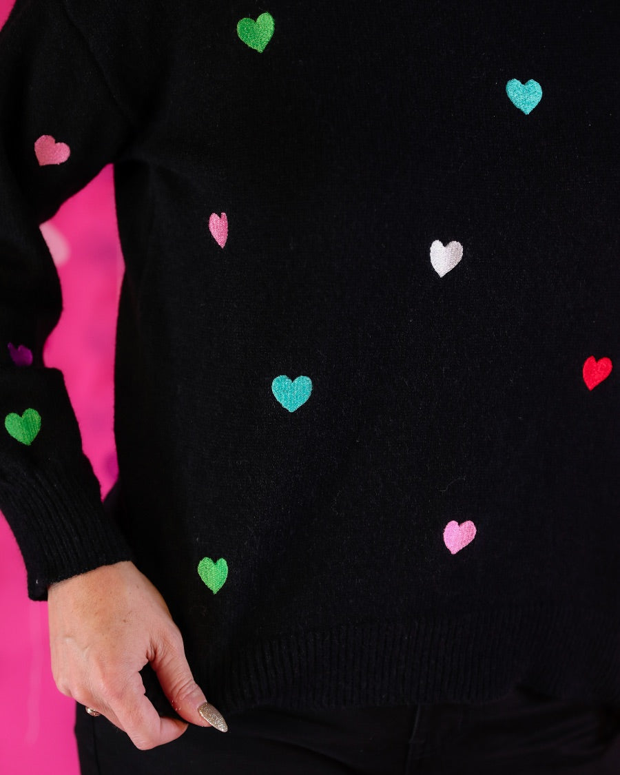 a black long-sleeve sweater crafted from snug, plush material adorned with colorful embroidered hearts, finished with ribbed trim on the neckline, cuffs, and hem