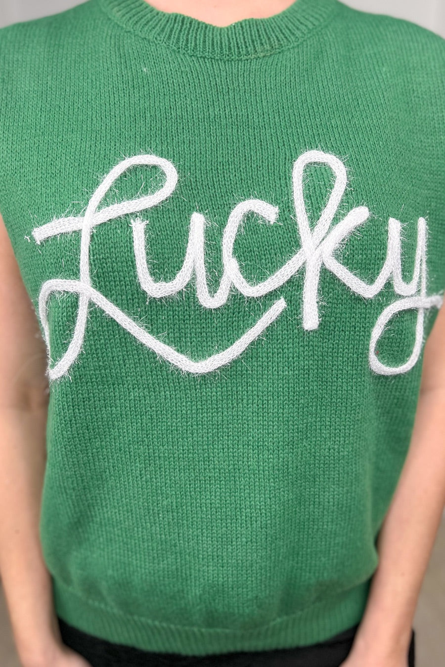 a green soft knit sleeveless seater vest with shimmering 'Lucky' lettering, a relaxed fit, and ribbed collar, cuffs, and hem
