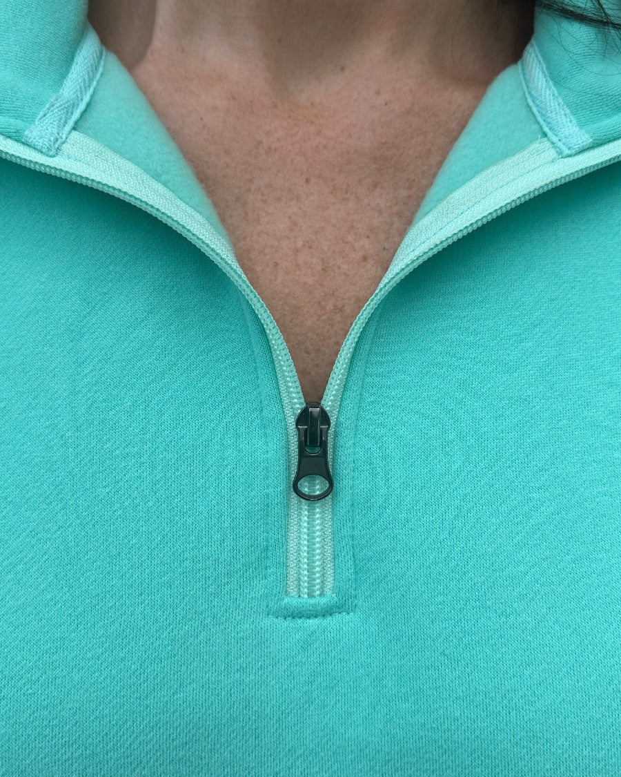 a long-sleeve pullover made of cozy fabric with a quarter zip, cuffs, and a split waistband hem in turquoise