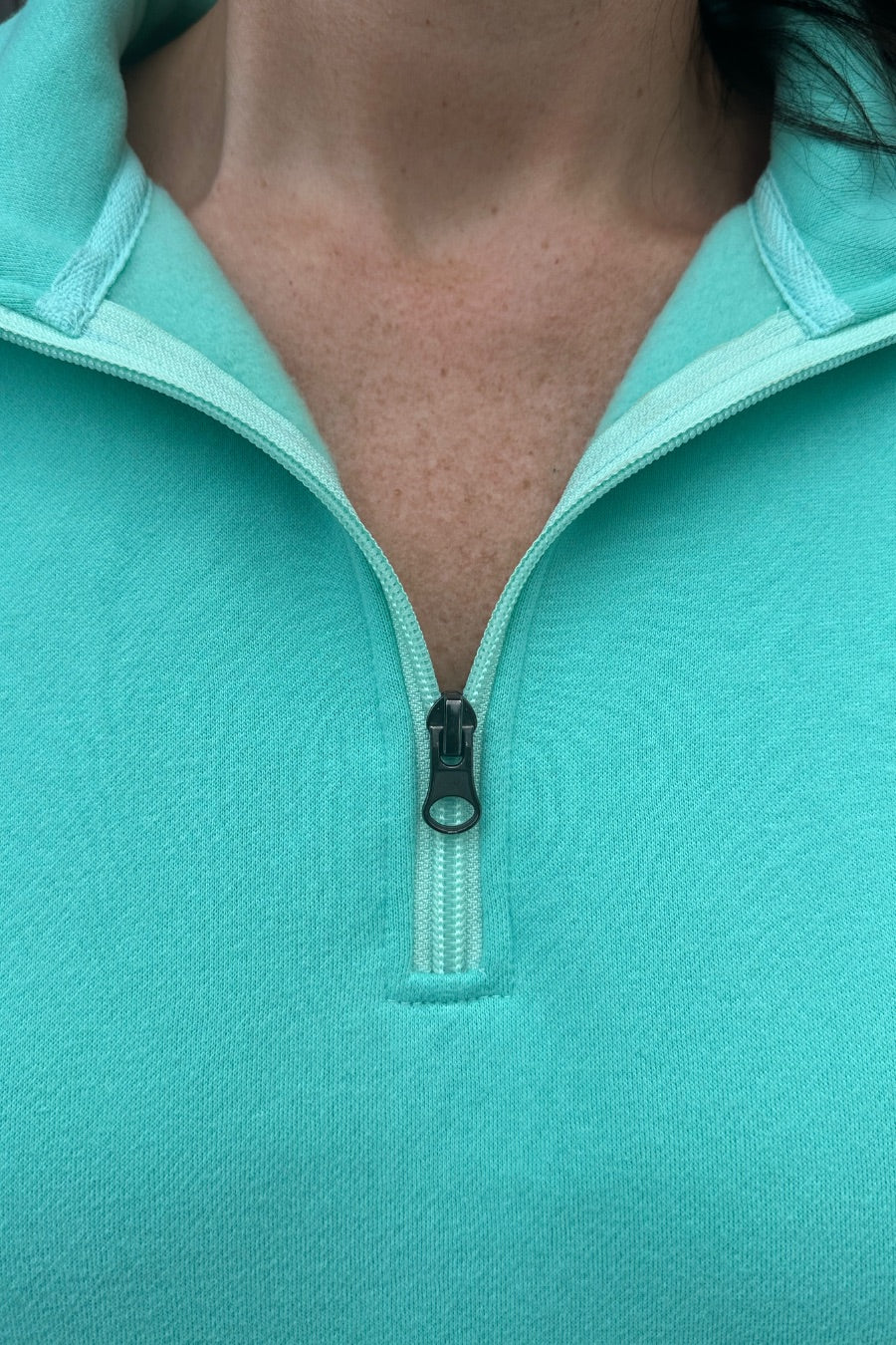 a long-sleeve pullover made of cozy fabric with a quarter zip, cuffs, and a split waistband hem in turquoise