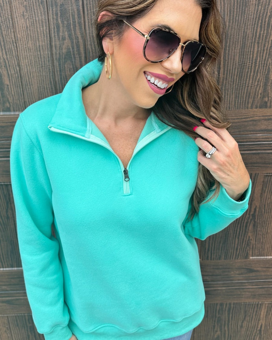 a long-sleeve pullover made of cozy fabric with a quarter zip, cuffs, and a split waistband hem in turquoise