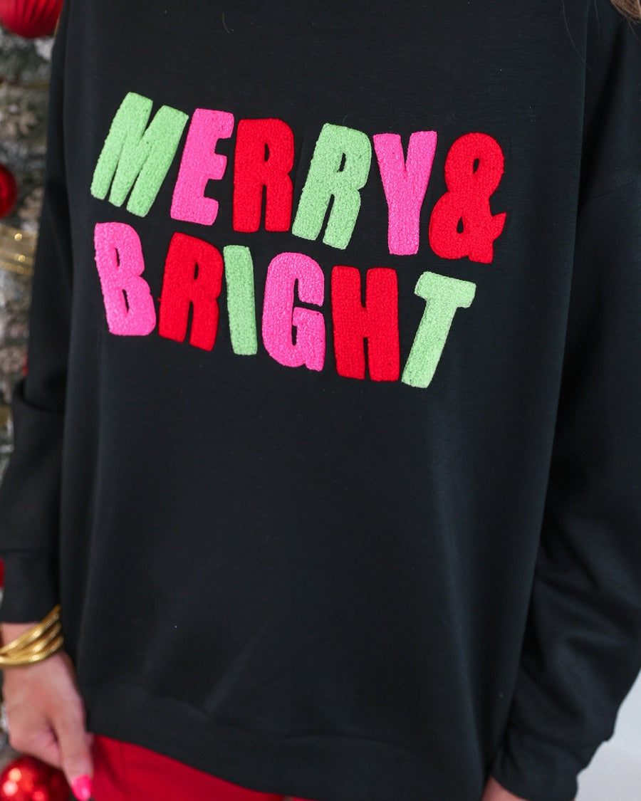 black long-sleeve sweatshirt with stitched chenille patches that spell out MERRY BRIGHT with an ampersand in between in alternating green, pink, and red on our new luxe material