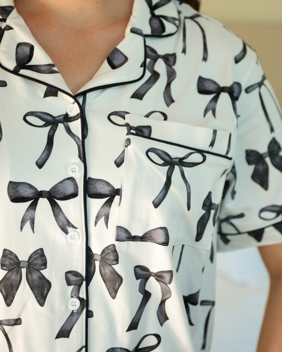short sleeve top and matching pants on white base with a black bow pattern, black piping, and black ruffle trim