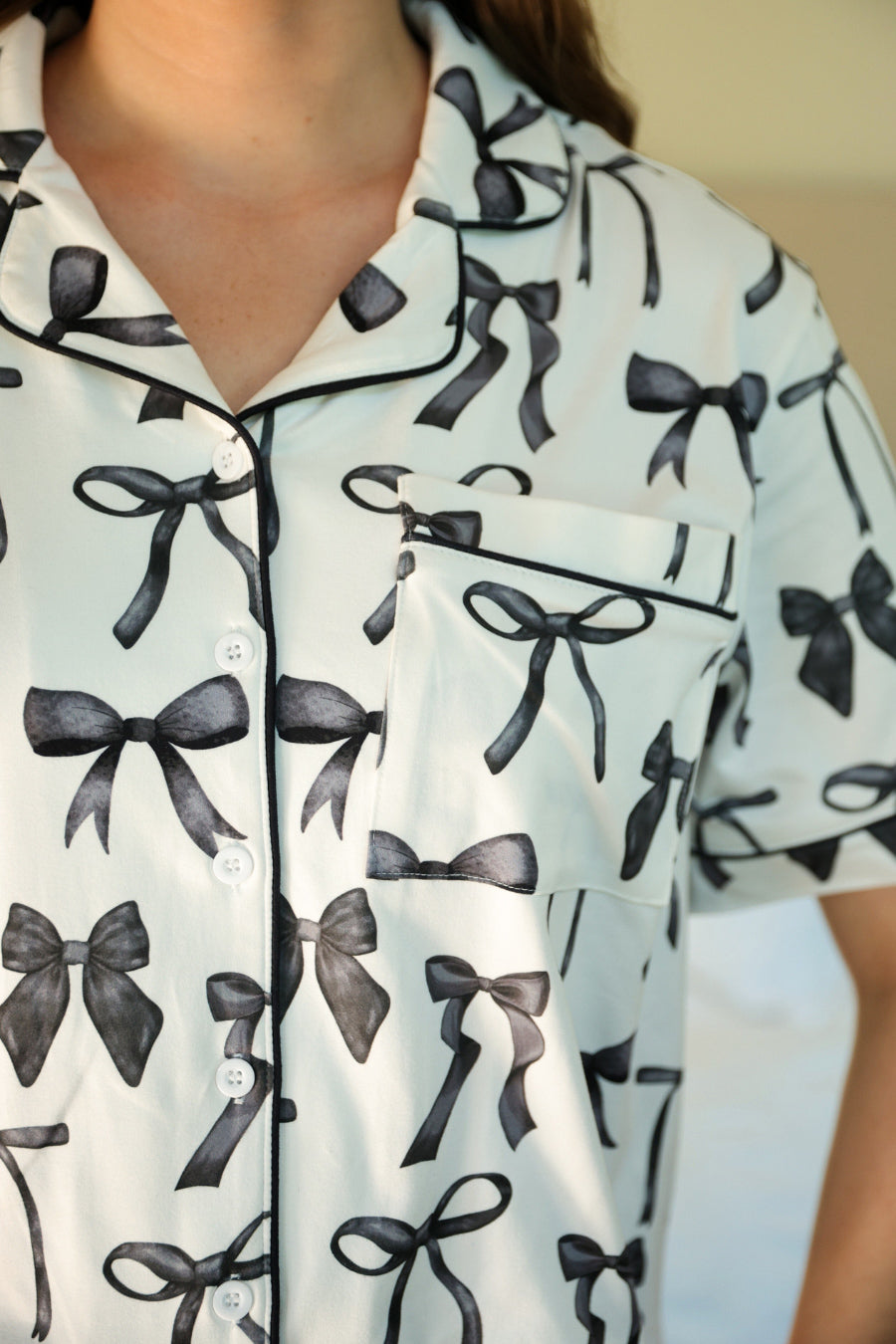 short sleeve top and matching pants on white base with a black bow pattern, black piping, and black ruffle trim