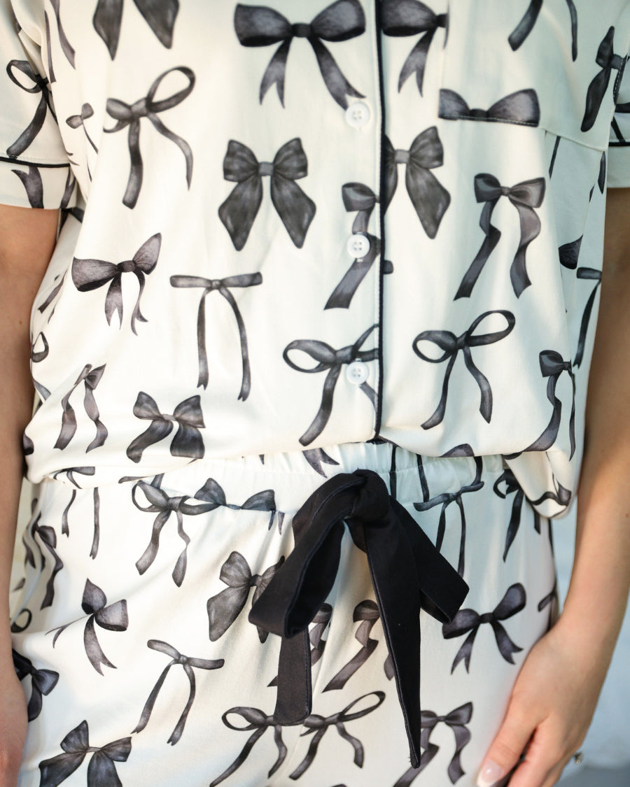 short sleeve top and matching pants on white base with a black bow pattern, black piping, and black ruffle trim