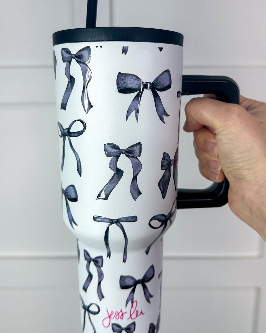 40-ounce white tumbler with a black bow and ribbon pattern print design, handle, screw-on lid, and a reusable straw