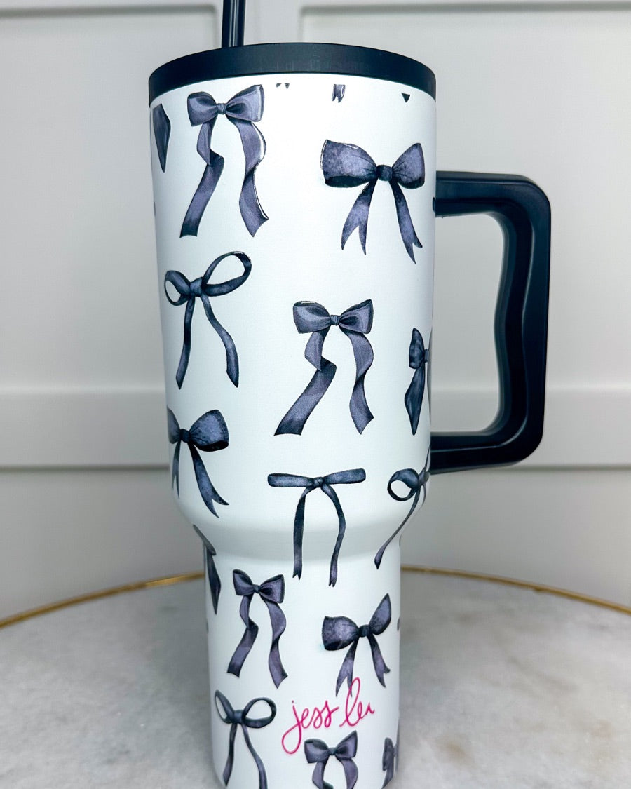 40-ounce white tumbler with a black bow and ribbon pattern print design, handle, screw-on lid, and a reusable straw