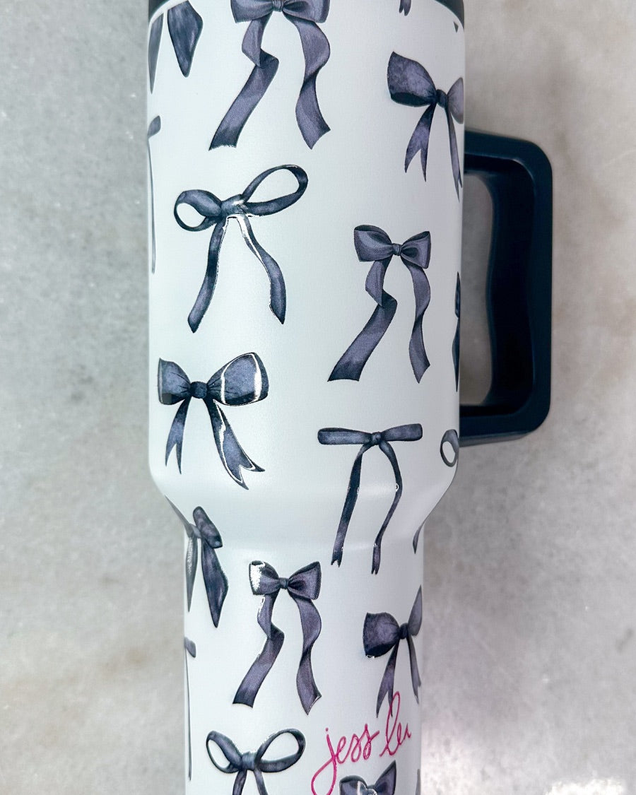 40-ounce white tumbler with a black bow and ribbon pattern print design, handle, screw-on lid, and a reusable straw