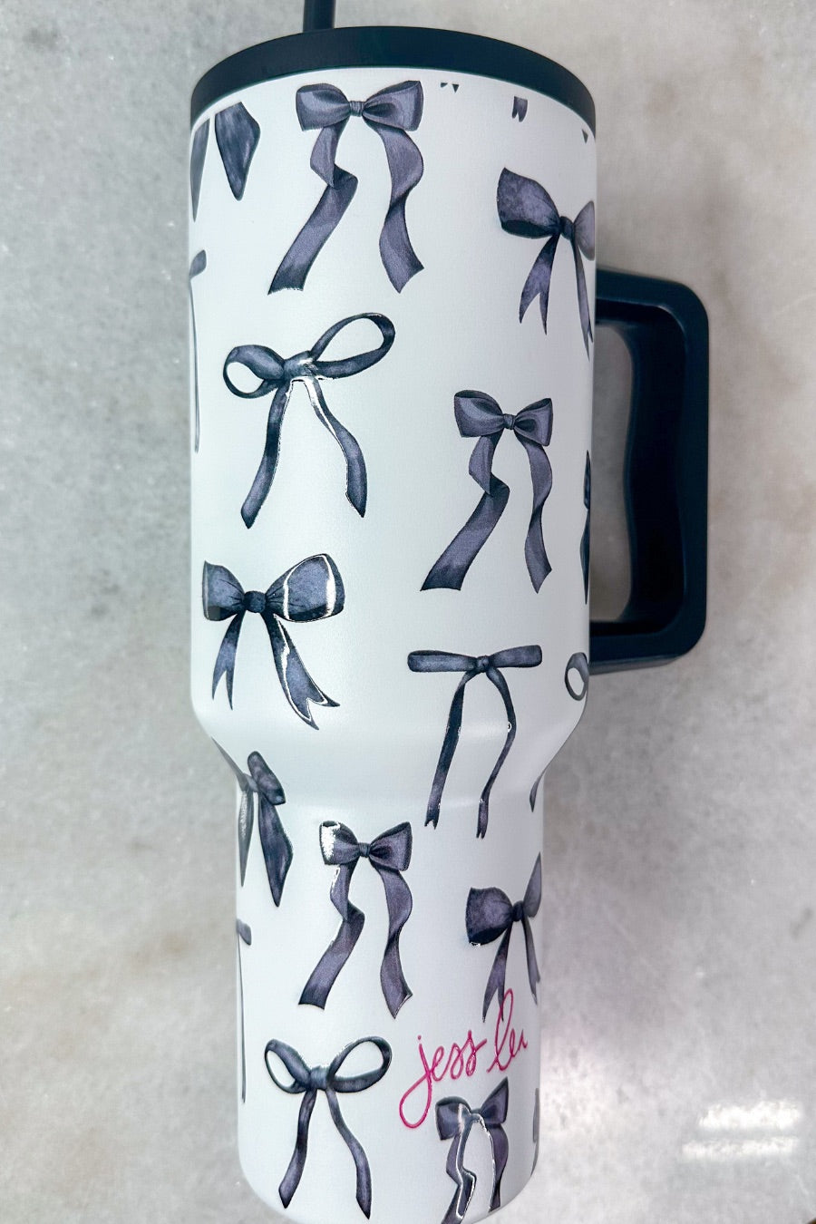 40-ounce white tumbler with a black bow and ribbon pattern print design, handle, screw-on lid, and a reusable straw