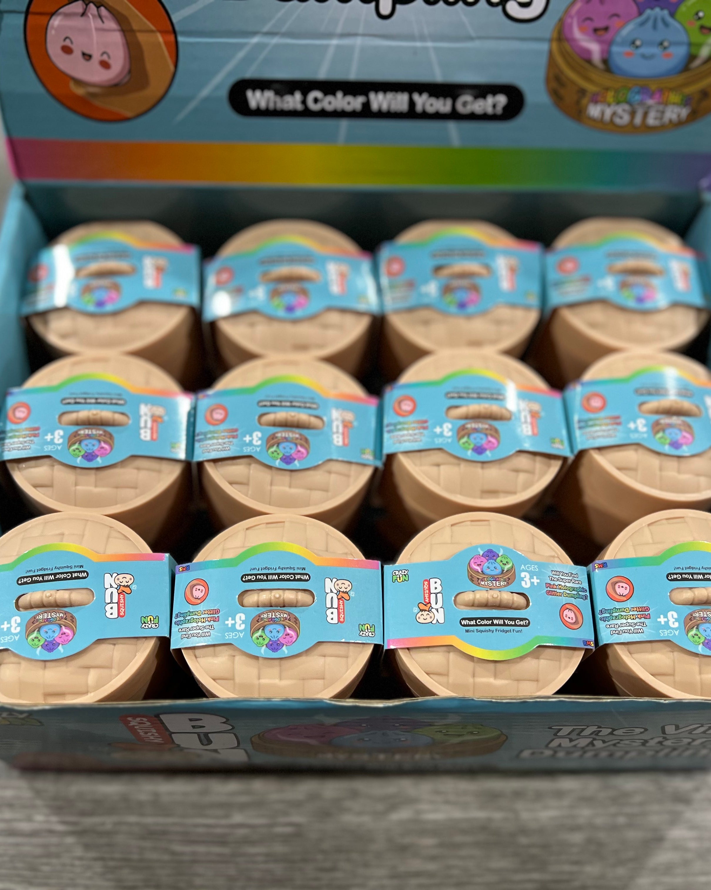 A retail display box filled with multiple small round mystery toy containers. The box is light blue with colorful graphics and text including 'What Color Will You Get?' and 'Mystery'.