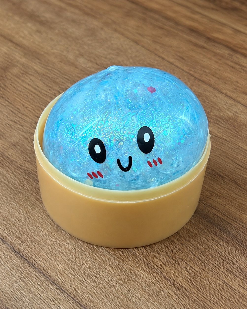 a blue mystery bead-filled mini dumpling squishy with assorted colors, iridescent shimmer, kawaii face, steamer-style container, and soft sensory texture
