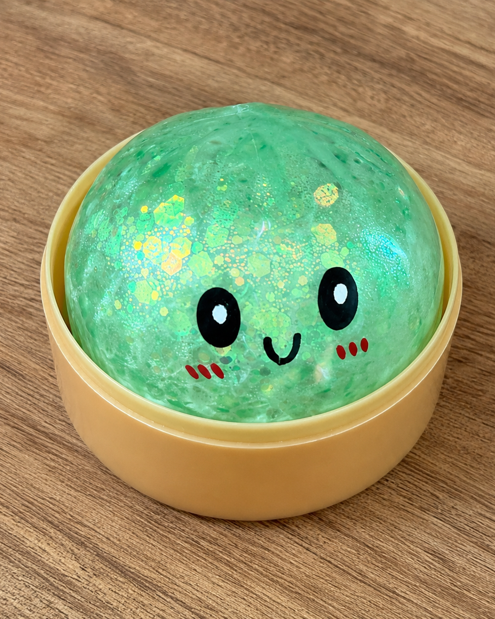 a green mystery bead-filled mini dumpling squishy with assorted colors, iridescent shimmer, kawaii face, steamer-style container, and soft sensory texture