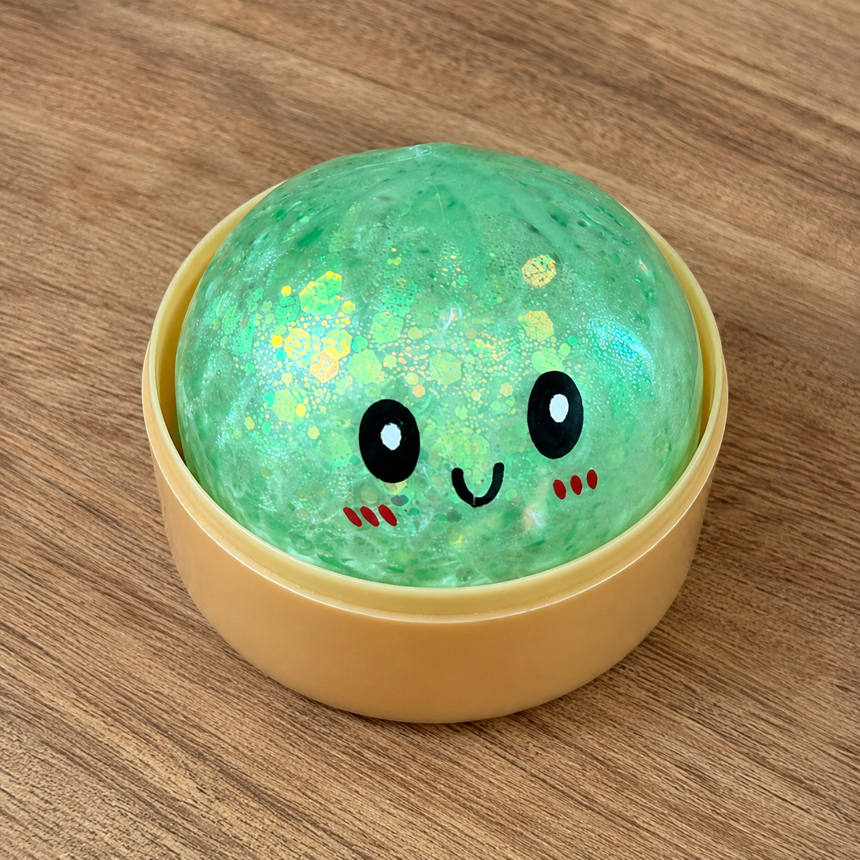 a green mystery bead-filled mini dumpling squishy with assorted colors, iridescent shimmer, kawaii face, steamer-style container, and soft sensory texture