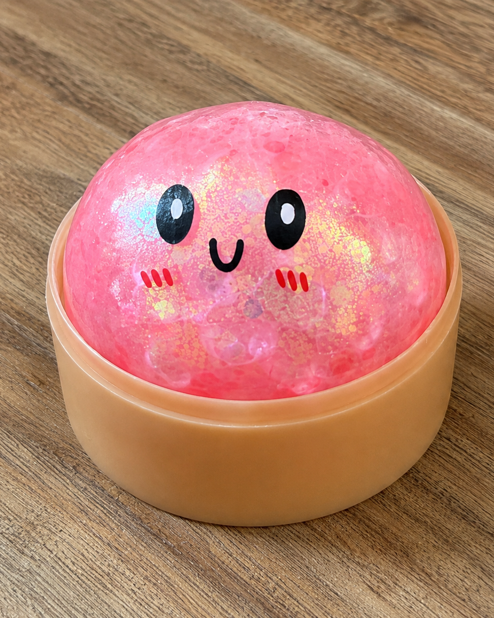 a pink mystery bead-filled mini dumpling squishy with assorted colors, iridescent shimmer, kawaii face, steamer-style container, and soft sensory texture