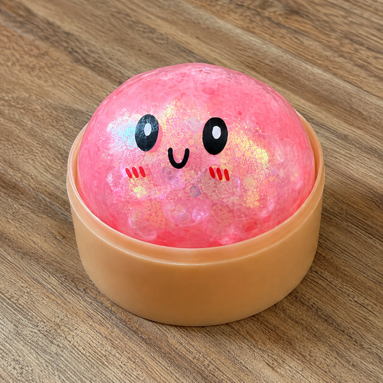 a pink mystery bead-filled mini dumpling squishy with assorted colors, iridescent shimmer, kawaii face, steamer-style container, and soft sensory texture