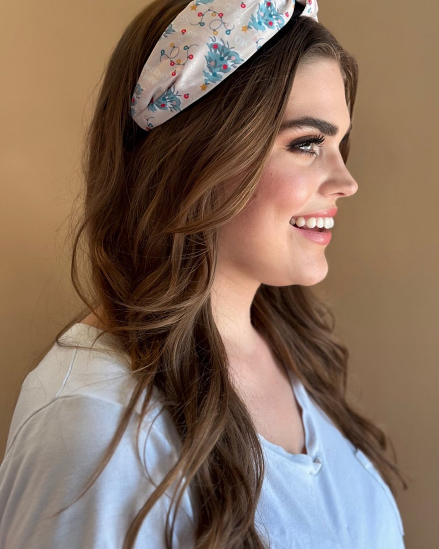 a twisted center knot crafted from lightweight fabric with holiday pattern print including Christmas trees, twinkling string lights, ornaments, and a 'ho ho ho' print 