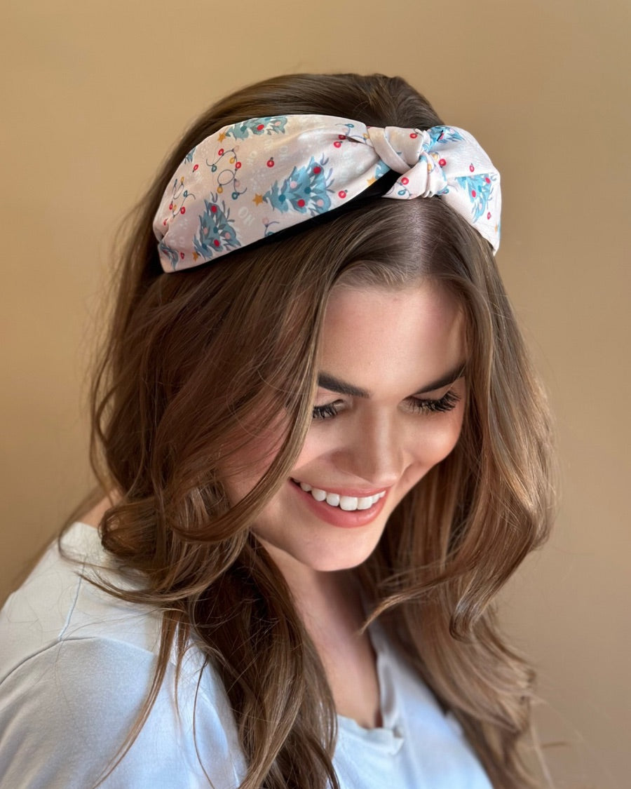 a twisted center knot crafted from lightweight fabric with holiday pattern print including Christmas trees, twinkling string lights, ornaments, and a 'ho ho ho' print 