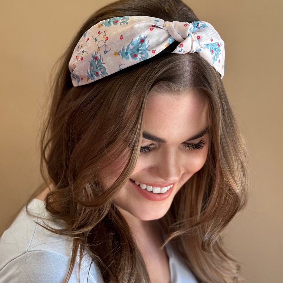 a twisted center knot crafted from lightweight fabric with holiday pattern print including Christmas trees, twinkling string lights, ornaments, and a 'ho ho ho' print 