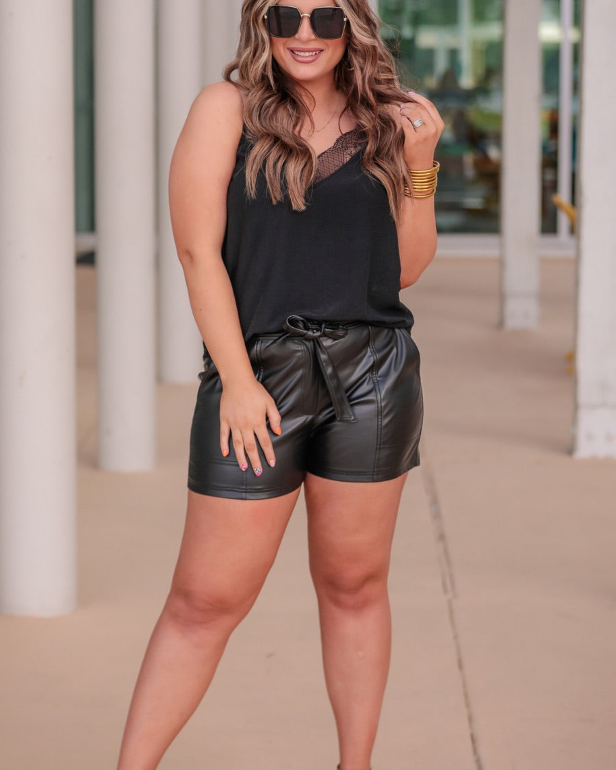 sleek faux leather shorts with zip and button closure, side pockets, a non-removable tie detail, and an elastic back waistband in black