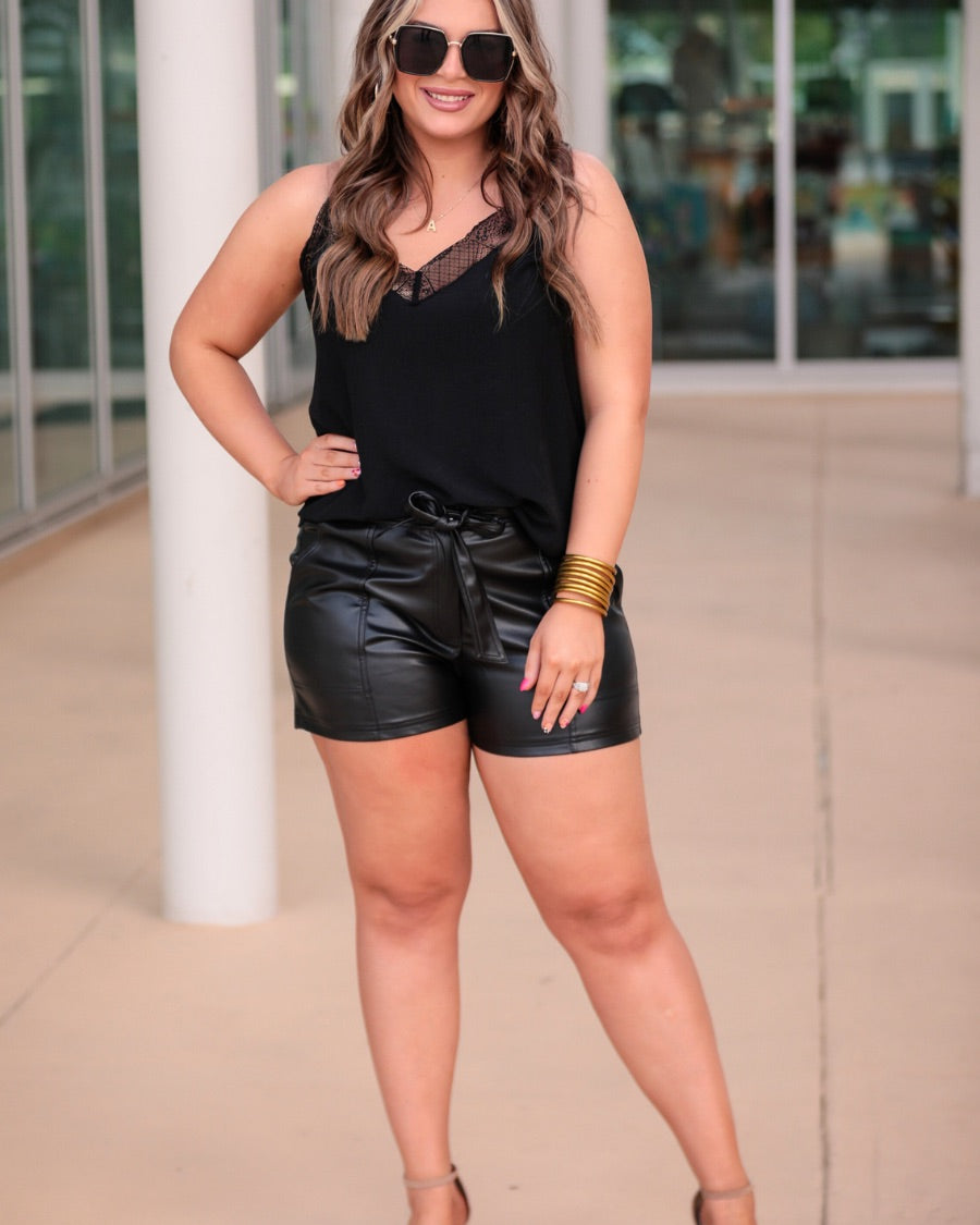 sleek faux leather shorts with zip and button closure, side pockets, a non-removable tie detail, and an elastic back waistband in black