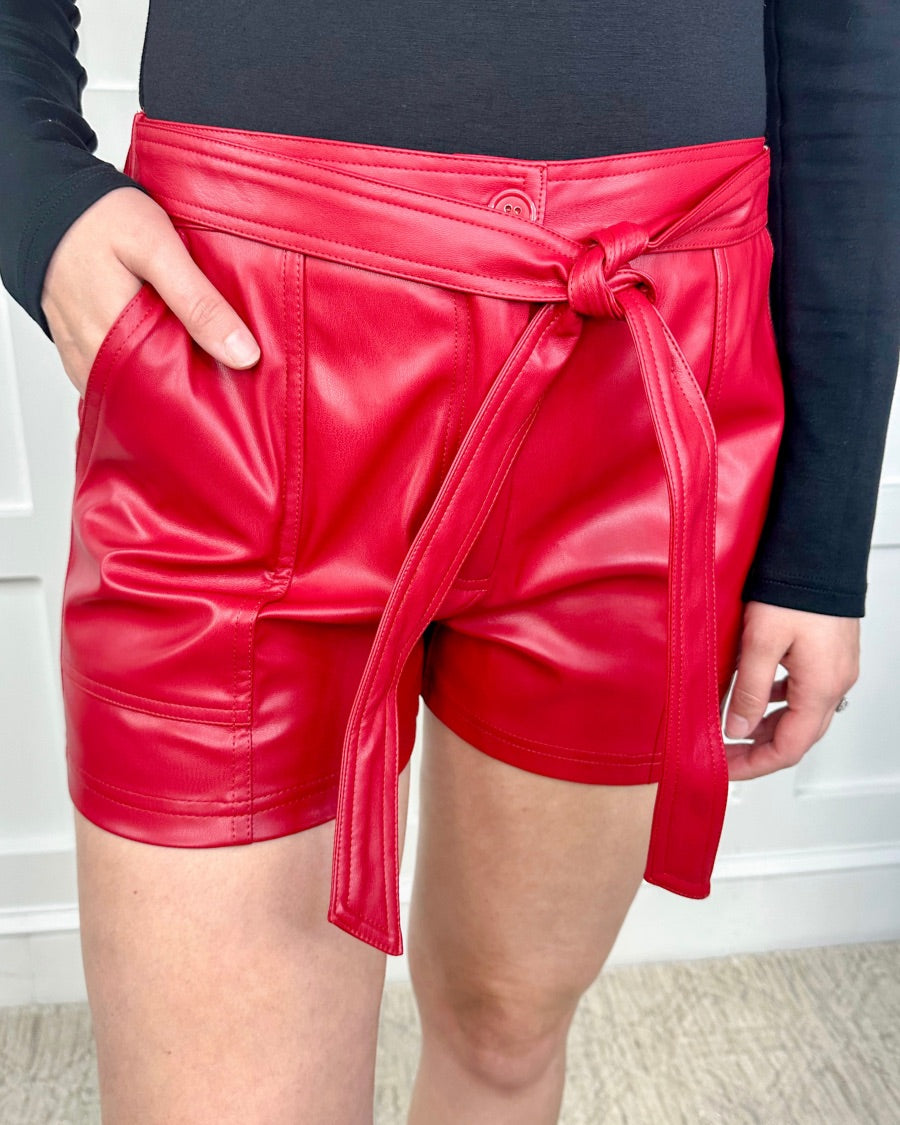 sleek faux leather shorts with zip and button closure, side pockets, a non-removable tie detail, and an elastic back waistband in red
