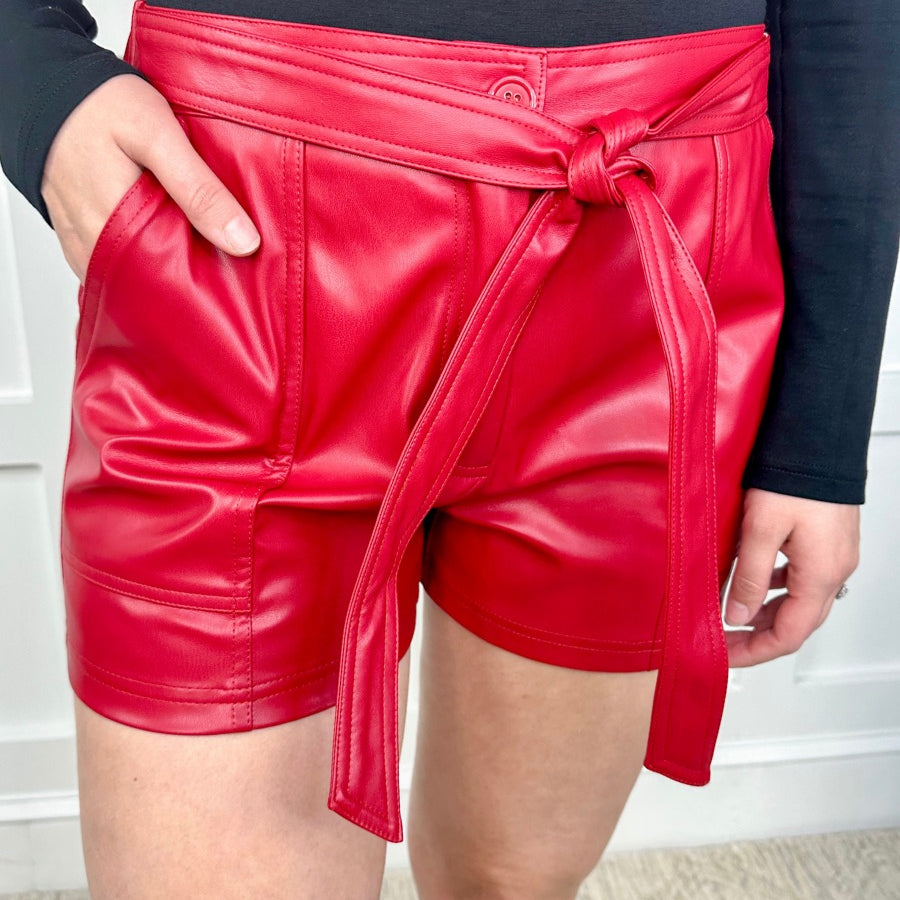 sleek faux leather shorts with zip and button closure, side pockets, a non-removable tie detail, and an elastic back waistband in red