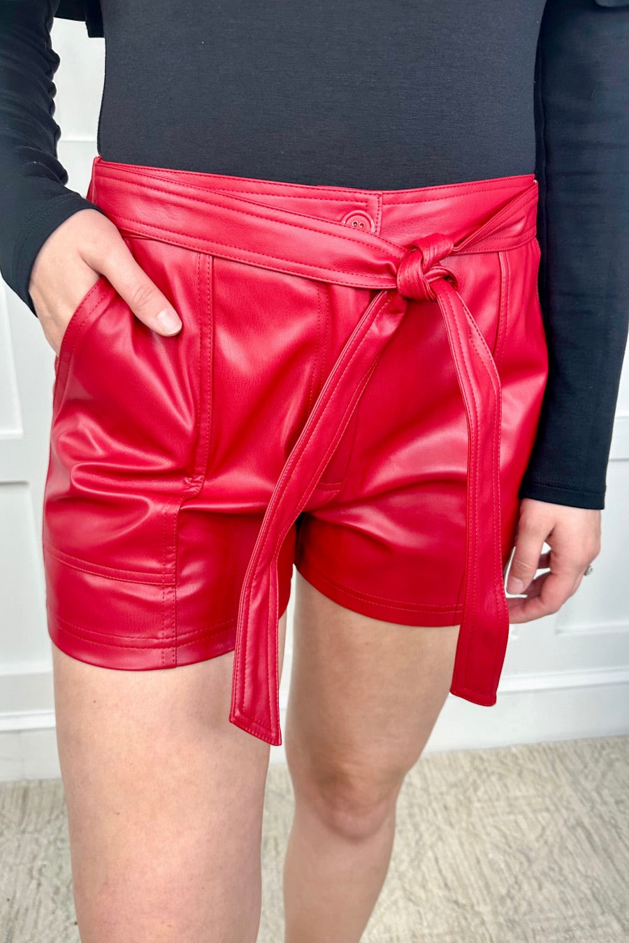 sleek faux leather shorts with zip and button closure, side pockets, a non-removable tie detail, and an elastic back waistband in red