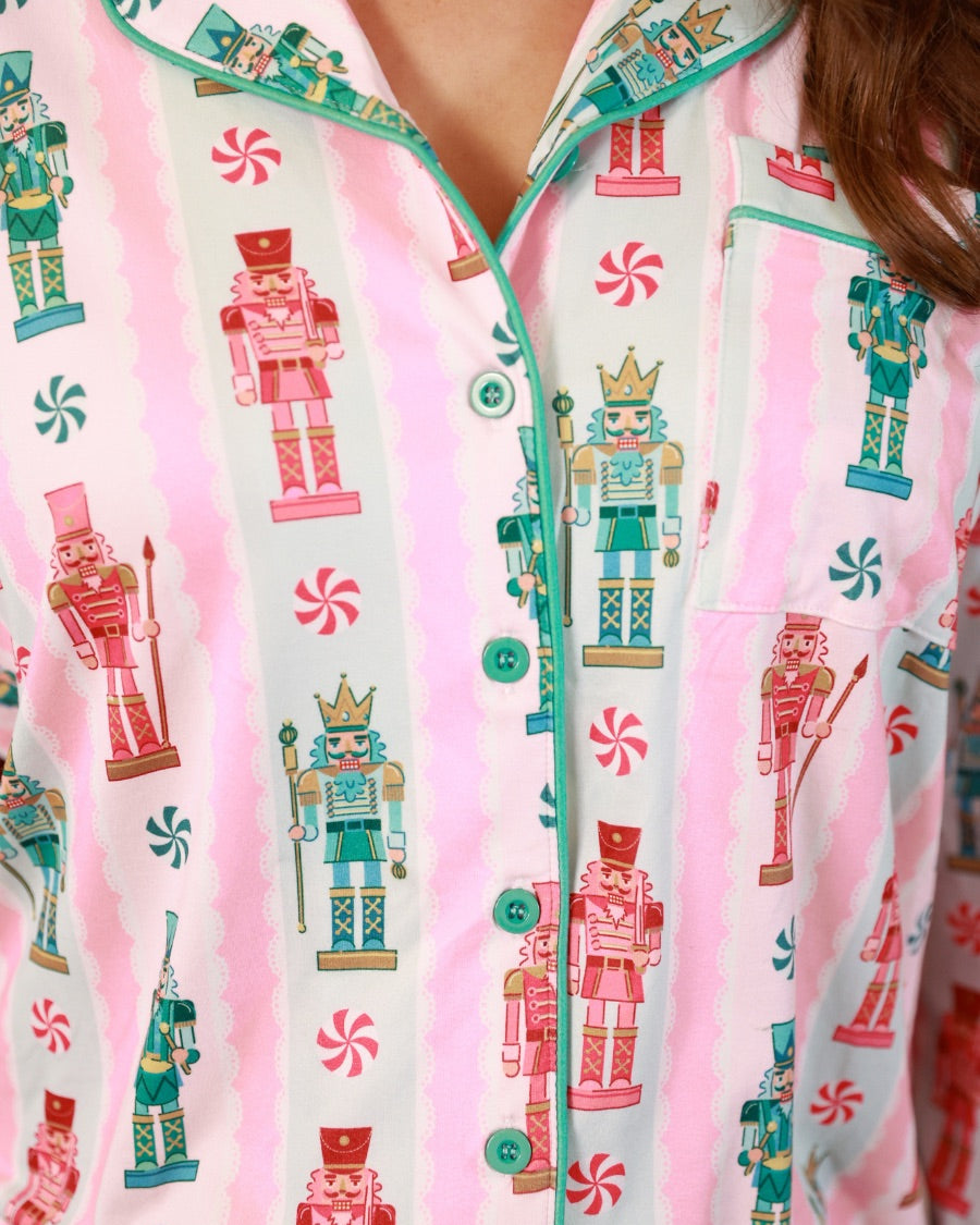 a soft two-piece pajama set (long sleeves and pants) with alternating nutcracker, peppermint, and aqua-and-pink stripe patterns, sweet ruffle hem detail, coordinating aqua trim accents, a decorative aqua faux belt, and a comfy elastic waistband for an easy, relaxed fit