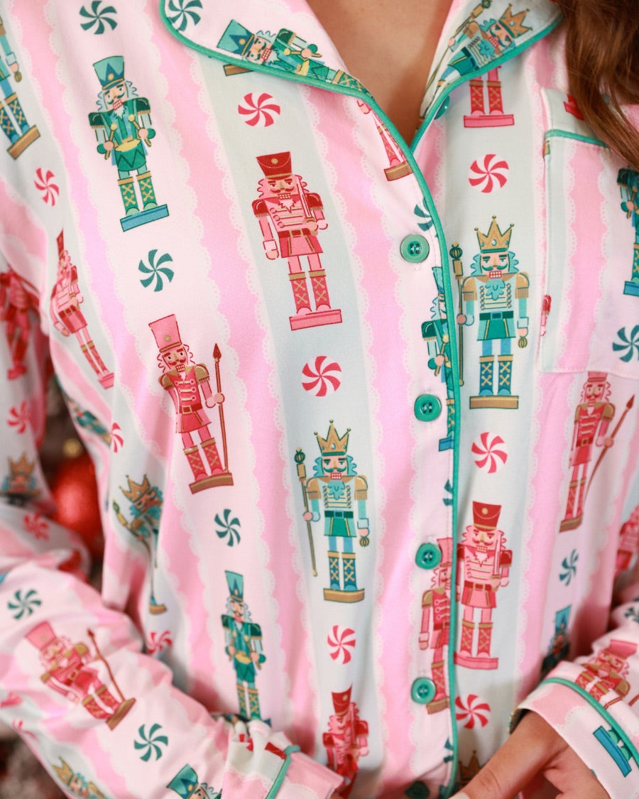 a soft two-piece pajama set (long sleeves and pants) with alternating nutcracker, peppermint, and aqua-and-pink stripe patterns, sweet ruffle hem detail, coordinating aqua trim accents, a decorative aqua faux belt, and a comfy elastic waistband for an easy, relaxed fit