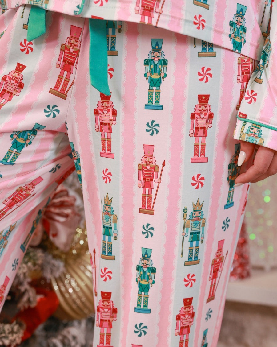 a soft two-piece pajama set (long sleeves and pants) with alternating nutcracker, peppermint, and aqua-and-pink stripe patterns, sweet ruffle hem detail, coordinating aqua trim accents, a decorative aqua faux belt, and a comfy elastic waistband for an easy, relaxed fit