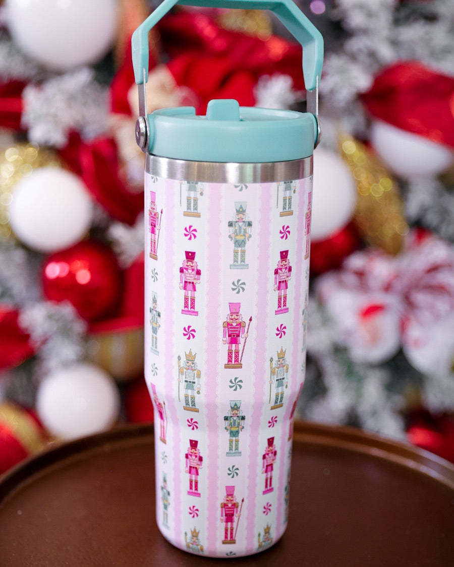 30-ounce striped pale pink insulated tumbler with a variety of whimsical multicolor pastel nutcrackers and peppermint swirls on white lace with a mint sturdy built-in handle, lid, and straw complete with silver hardware