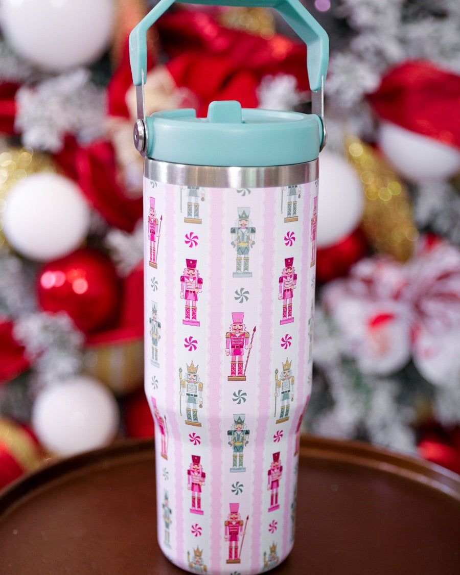 30-ounce striped pale pink insulated tumbler with a variety of whimsical multicolor pastel nutcrackers and peppermint swirls on white lace with a mint sturdy built-in handle, lid, and straw complete with silver hardware