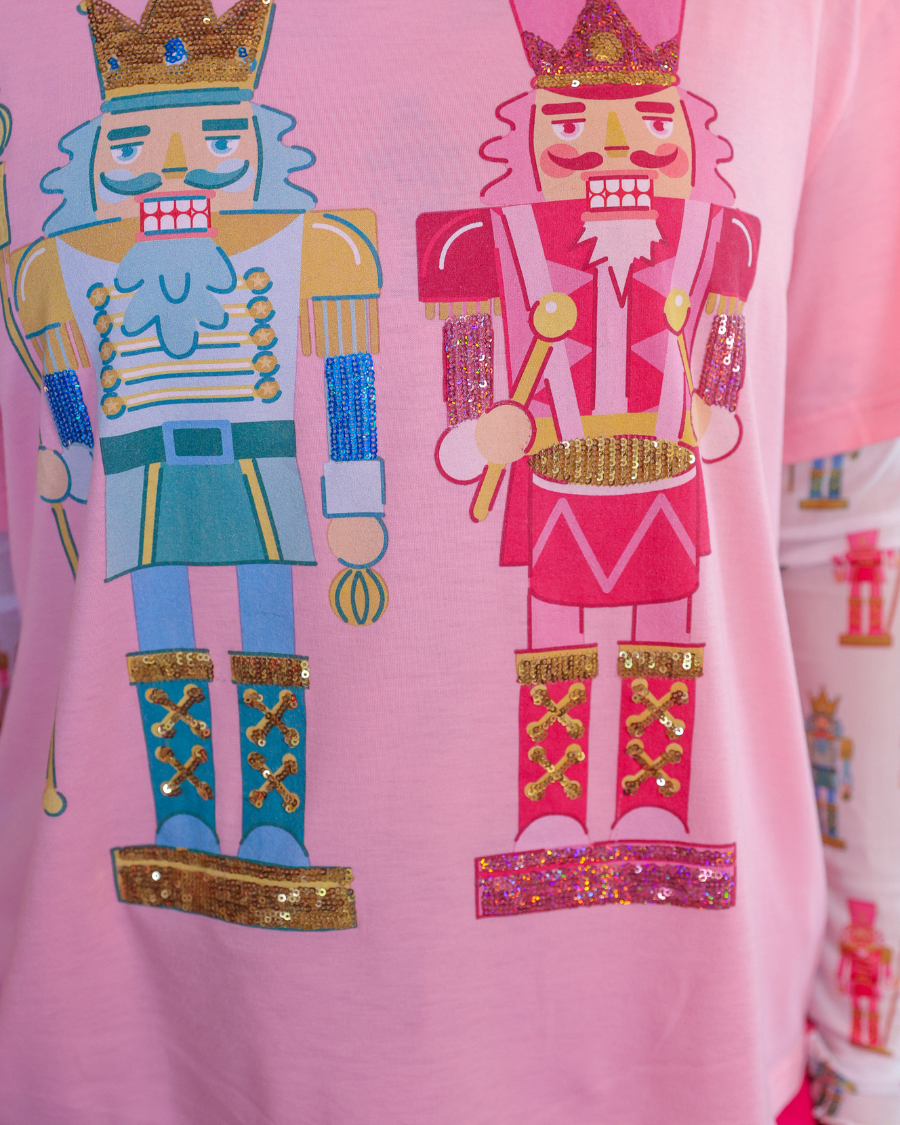 an oversized soft pink tee with sparkling multicolor sequin-embroidered nutcrackers, a contrasting aqua collar, and a relaxed fit