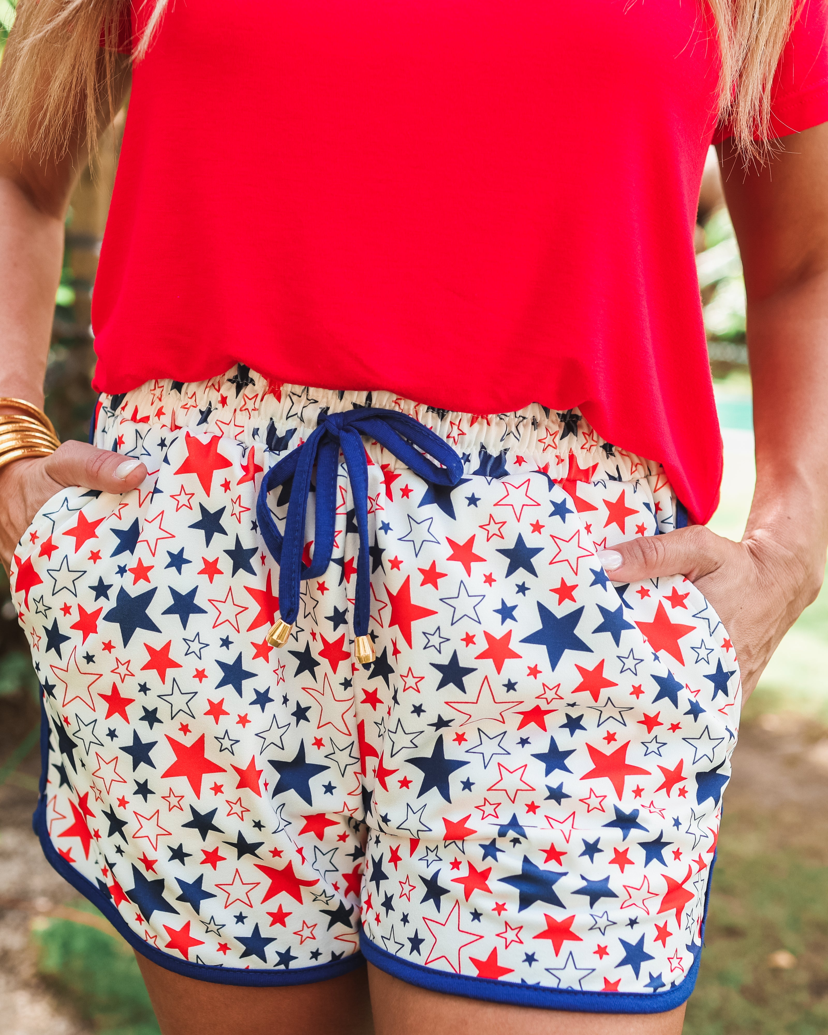 mid-rise relaxed fit activewear shorts with side pockets and a tie waist drawstring with gold bead accents, designed on a patriotic star pattern print fabric, white base, and navy trim
