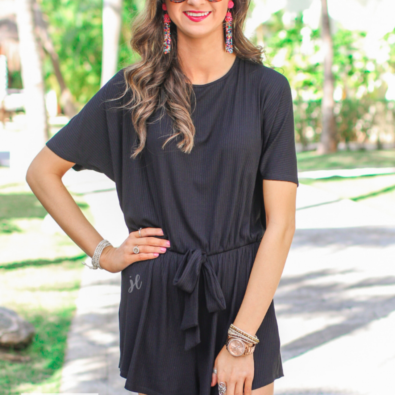 a black short-sleeve ribbed romper with a scoop neckline, a cutout tie back, an elastic waist with a faux tie detail, no pockets, and a relaxed, lightweight fit, accented with a MADE IN USA watermark in bottom left-hand corner