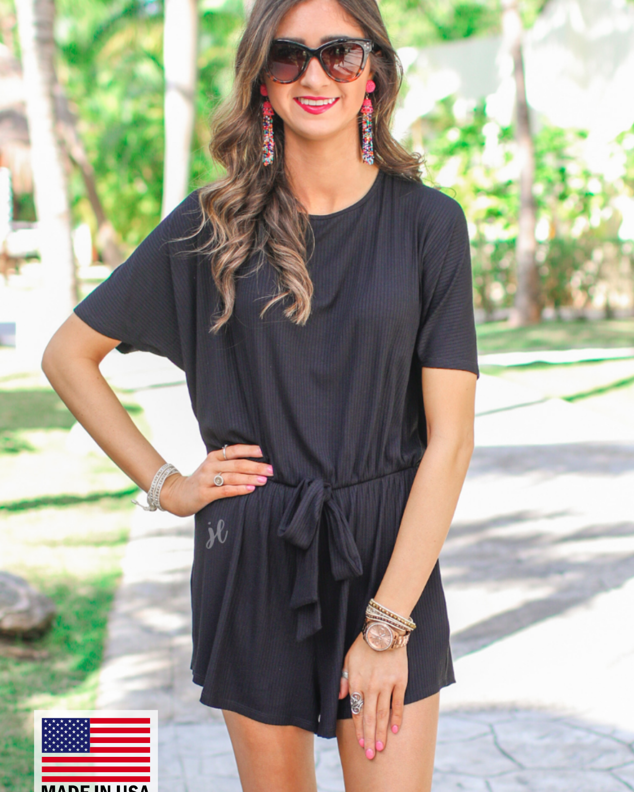 a black short-sleeve ribbed romper with a scoop neckline, a cutout tie back, an elastic waist with a faux tie detail, no pockets, and a relaxed, lightweight fit, accented with a MADE IN USA watermark in bottom left-hand corner
