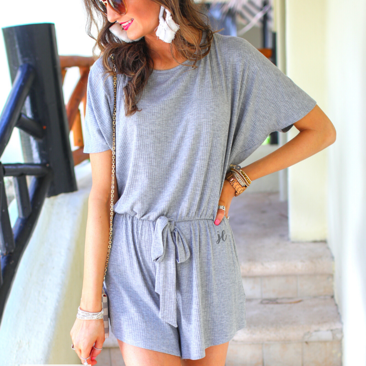 a grey short-sleeve ribbed romper with a scoop neckline, a cutout tie back, an elastic waist with a faux tie detail, no pockets, and a relaxed, lightweight fit, accented with a MADE IN USA watermark in bottom left-hand corner