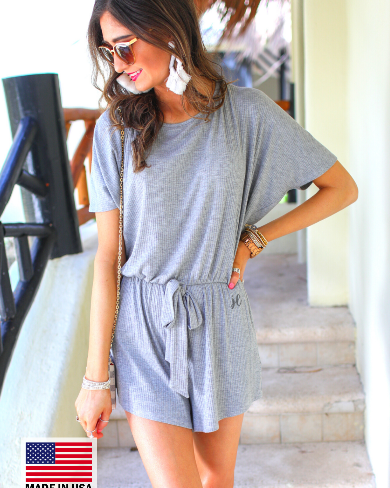 a grey short-sleeve ribbed romper with a scoop neckline, a cutout tie back, an elastic waist with a faux tie detail, no pockets, and a relaxed, lightweight fit, accented with a MADE IN USA watermark in bottom left-hand corner