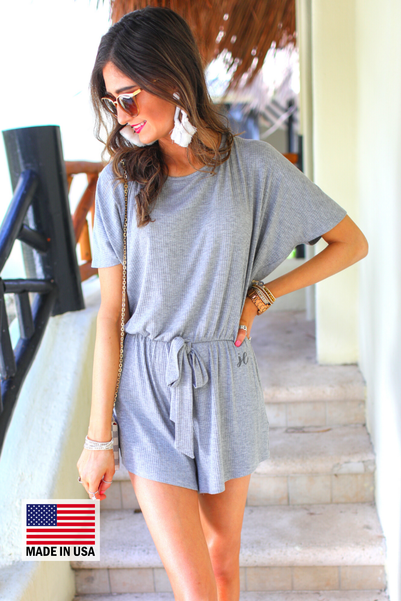 a grey short-sleeve ribbed romper with a scoop neckline, a cutout tie back, an elastic waist with a faux tie detail, no pockets, and a relaxed, lightweight fit, accented with a MADE IN USA watermark in bottom left-hand corner