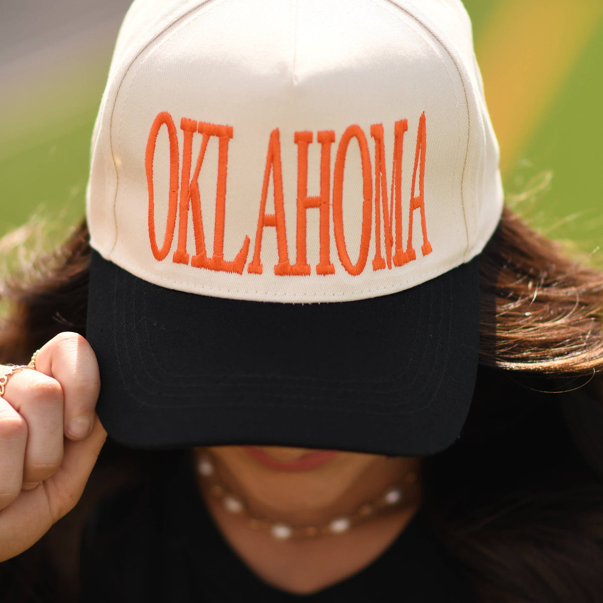 a lightweight unisex two-tone hat with embroidered orange 'OKLAHOMA' lettering, cream structured front, curved contrasting black bill, orange top button, and adjustable snap-back closure