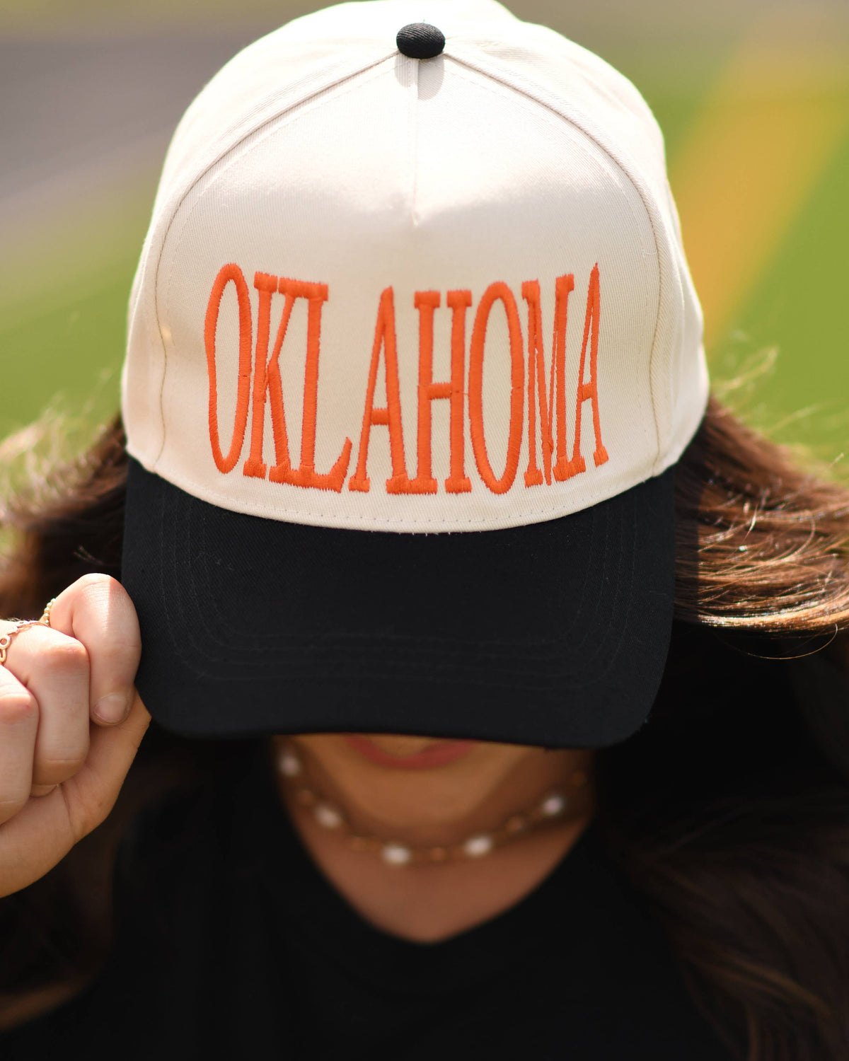a lightweight unisex two-tone hat with embroidered orange 'OKLAHOMA' lettering, cream structured front, curved contrasting black bill, orange top button, and adjustable snap-back closure
