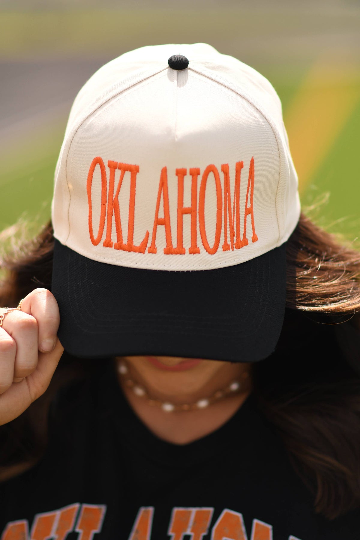 a lightweight unisex two-tone hat with embroidered orange 'OKLAHOMA' lettering, cream structured front, curved contrasting black bill, orange top button, and adjustable snap-back closure