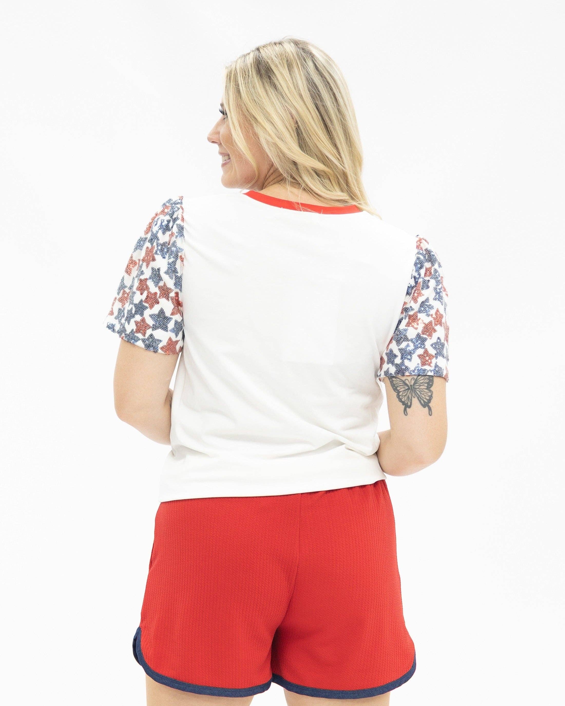 a high-stretch roomy-fit crew neck top with a sequin American flag front, lined star sleeves (red, white, and blue), red neckline trim, and a comfortable fit that runs large